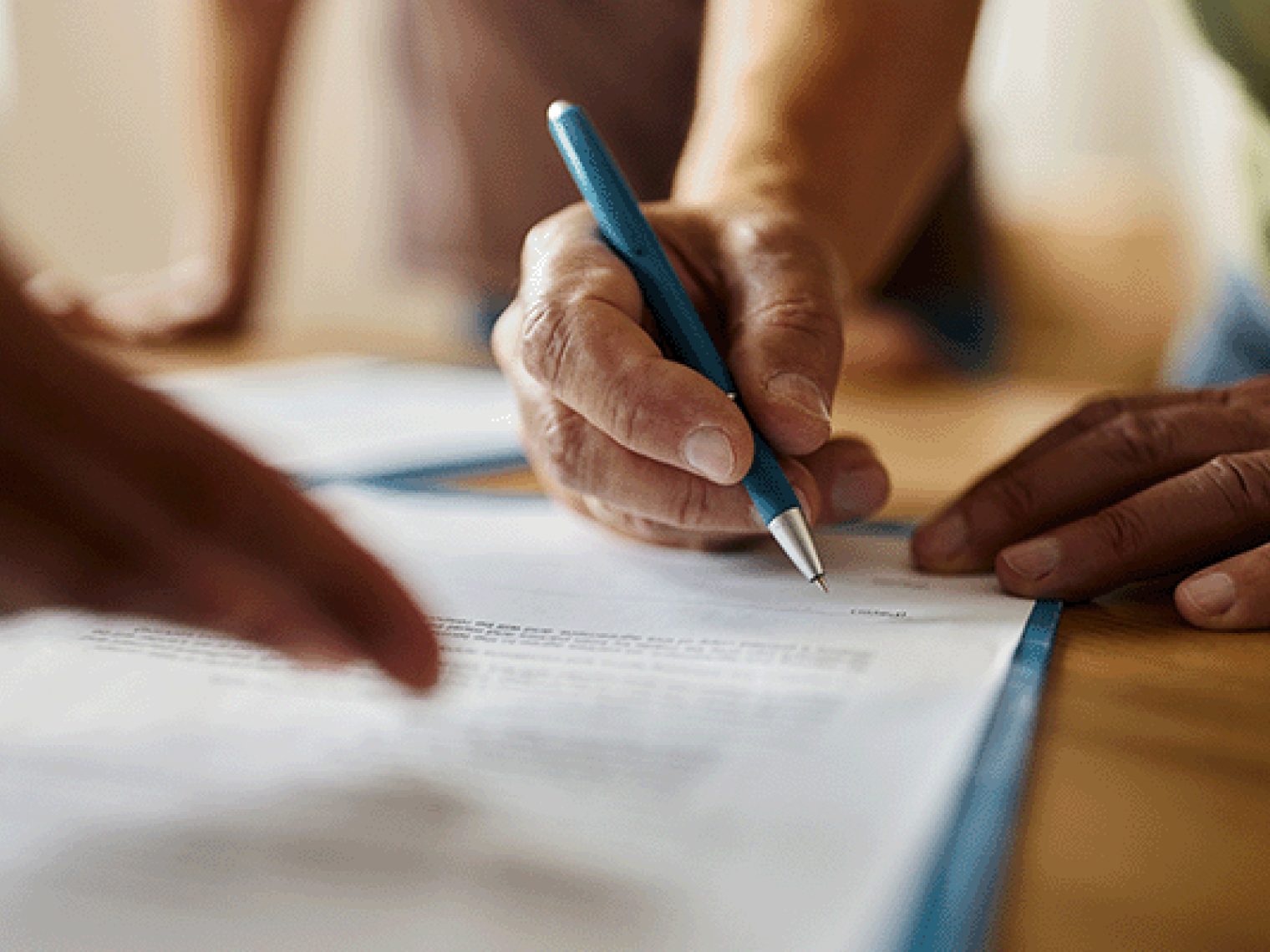 A close-up of someone signing a piece of paper with a blue pen on a table.