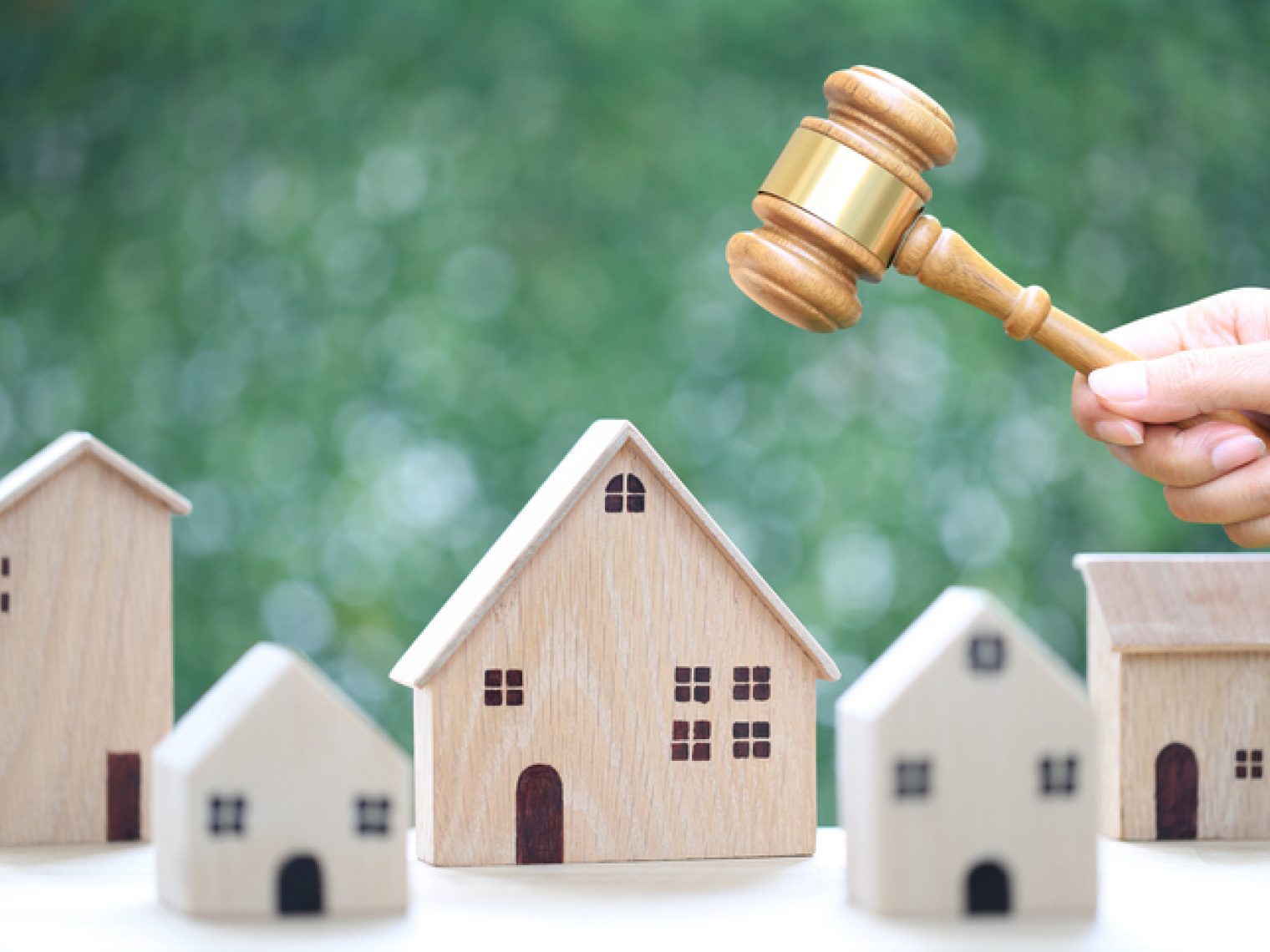 A hand holding a wooden auctioneer's gavel above miniature house models, symbolizing real estate auction.